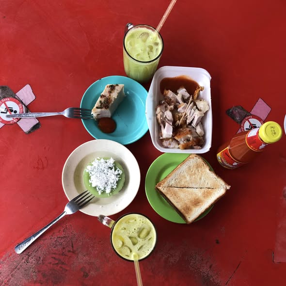 Breakfast on a red kopitiam table: drinks, toast and small dishes